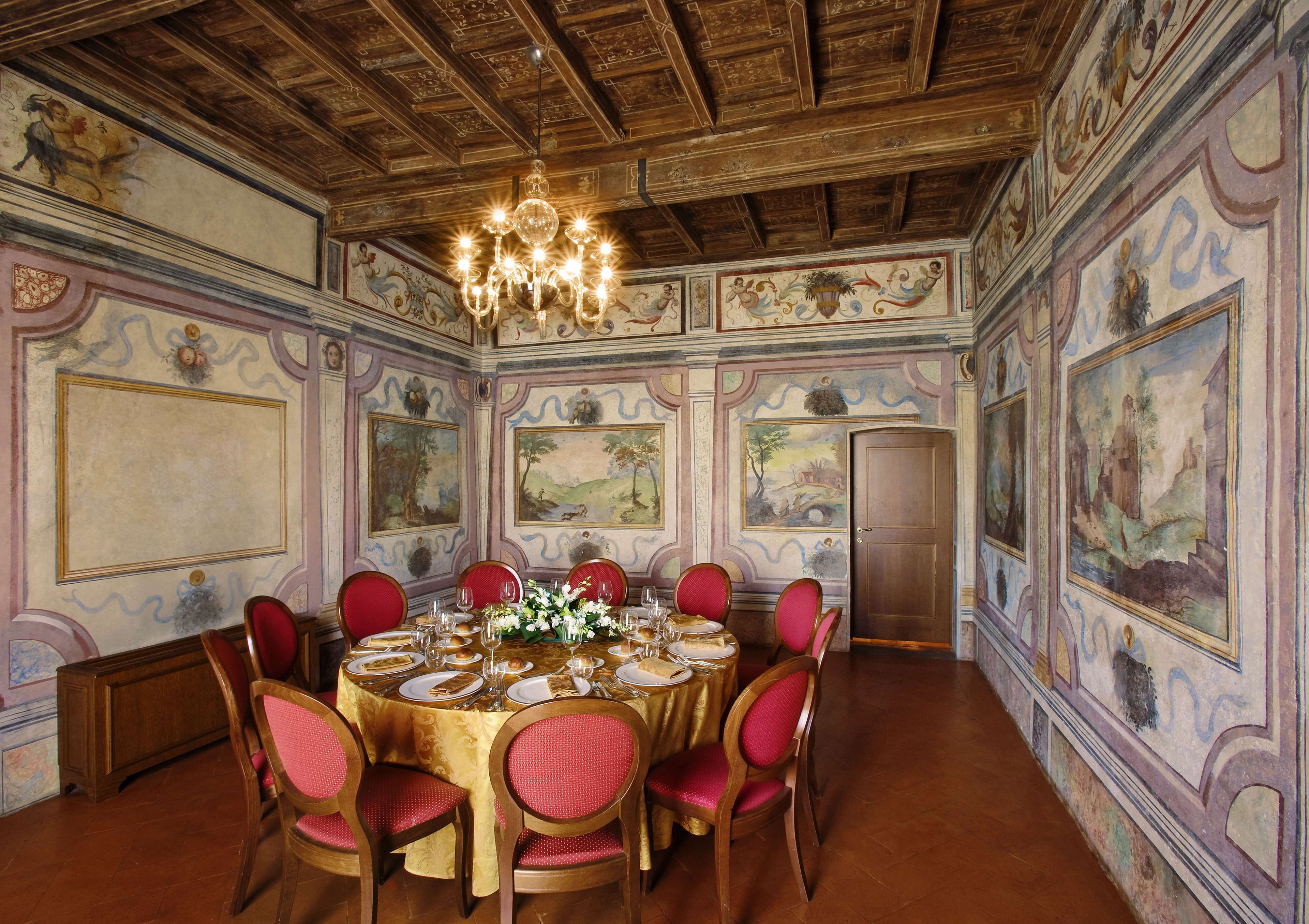 A dining room with a round table set for six, surrounded by red upholstered chairs.