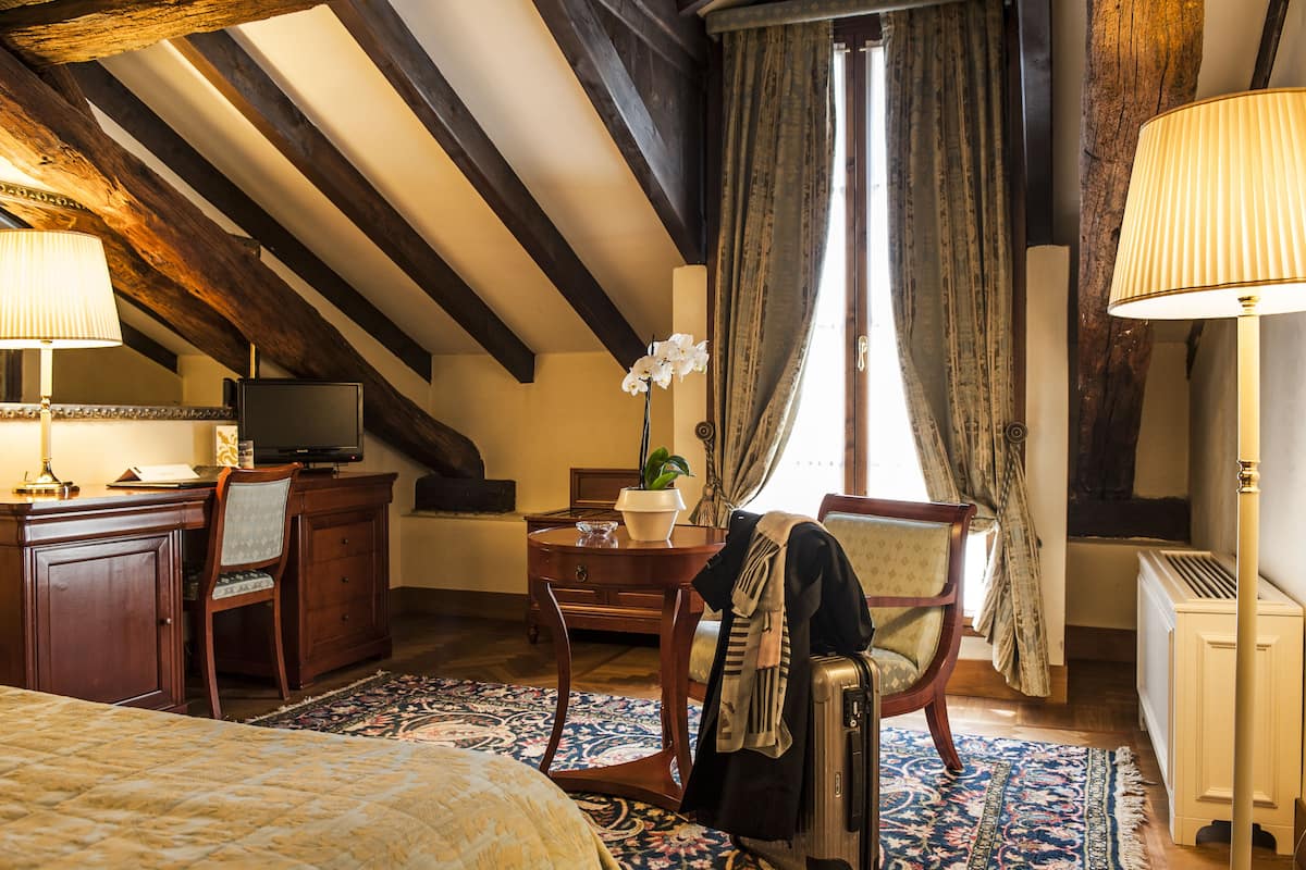 Ein Hotelzimmer mit einem Bett, einem Schreibtisch mit Lampe, einem Sessel, einem kleinen Tisch mit Pflanze und einer Heizung.