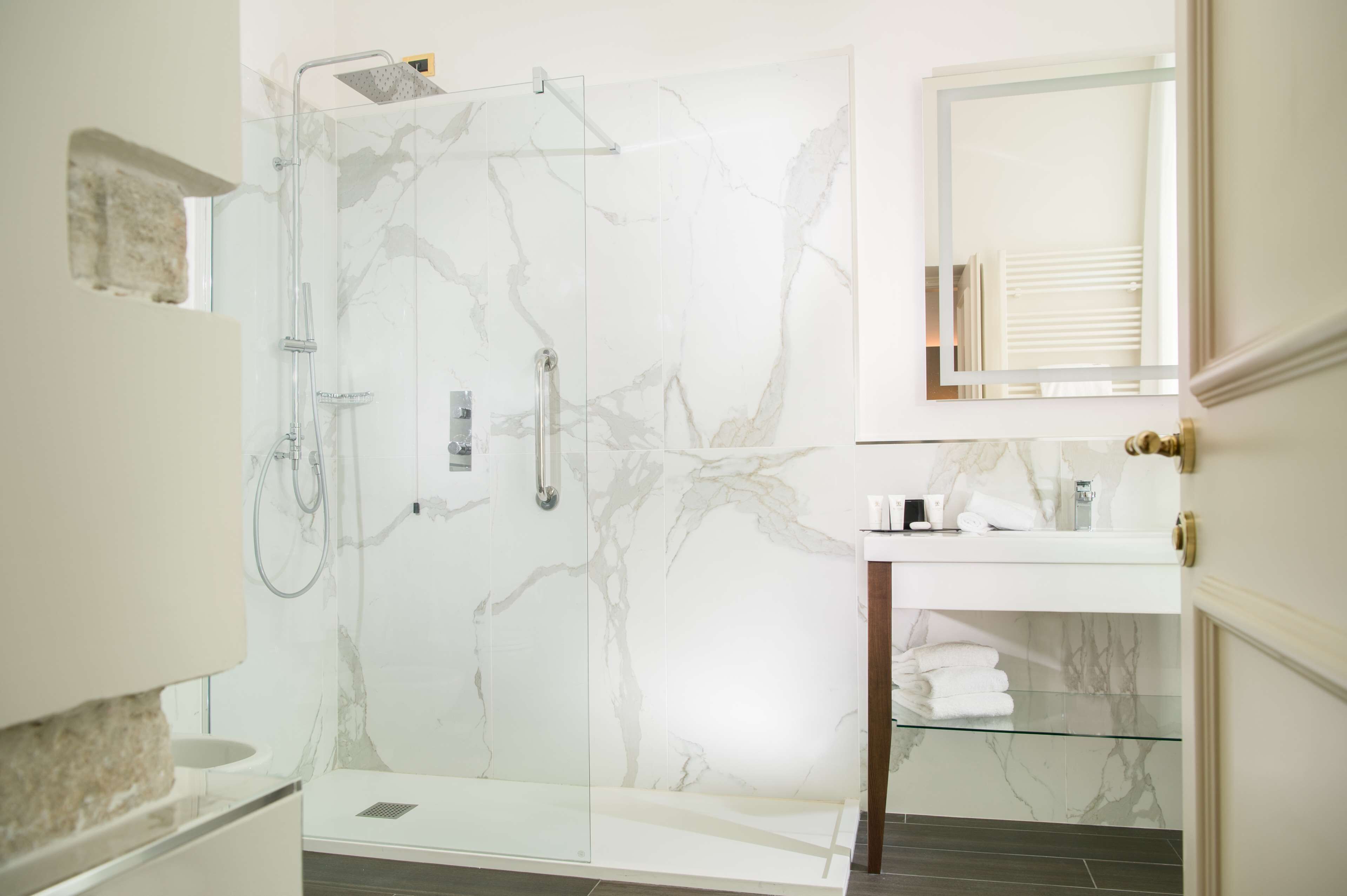Un bagno moderno con cabina doccia in vetro, pareti in marmo e mobile vanitario con piano in vetro.