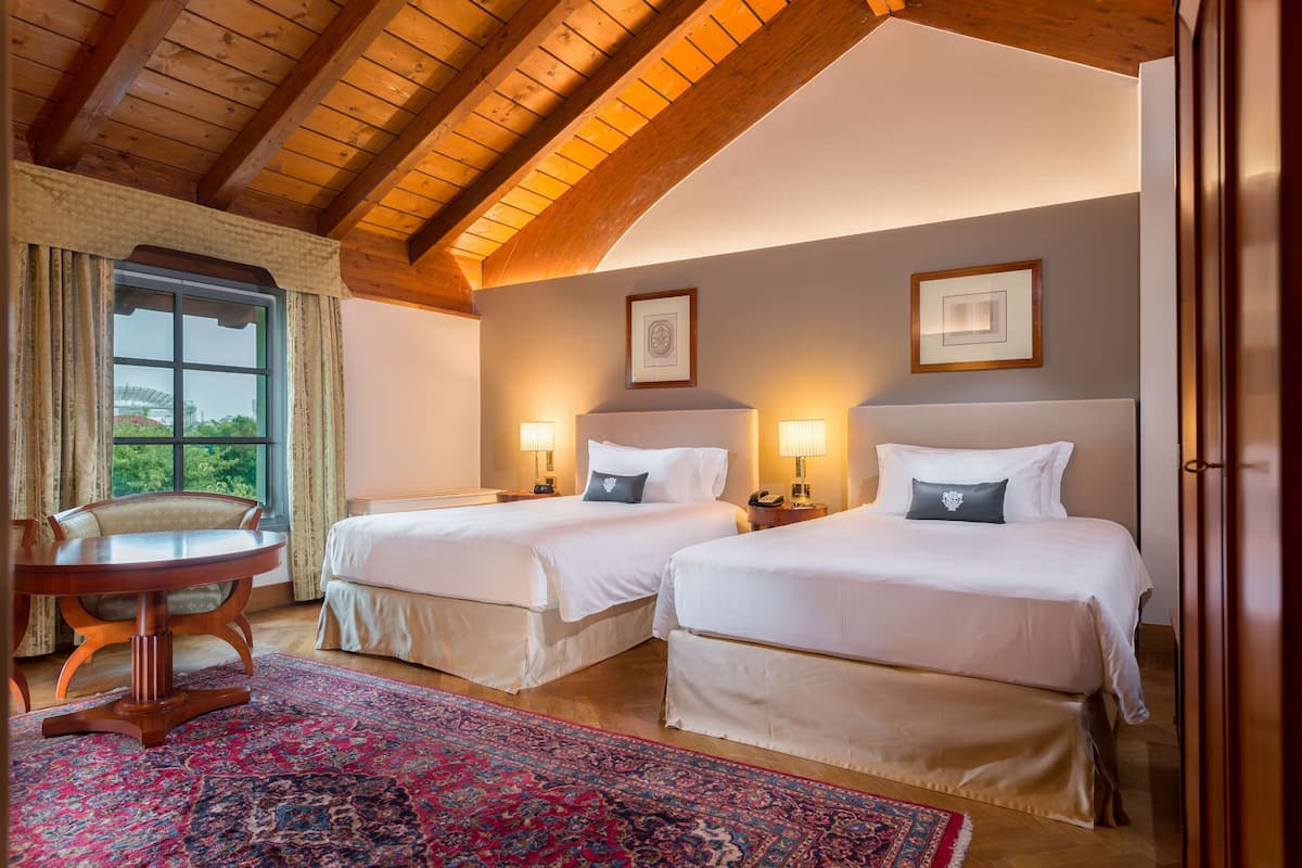 Ein Hotelzimmer mit zwei Betten, einer Holzbalkendecke, einem runden Tisch und einem großen Fenster mit Vorhängen.