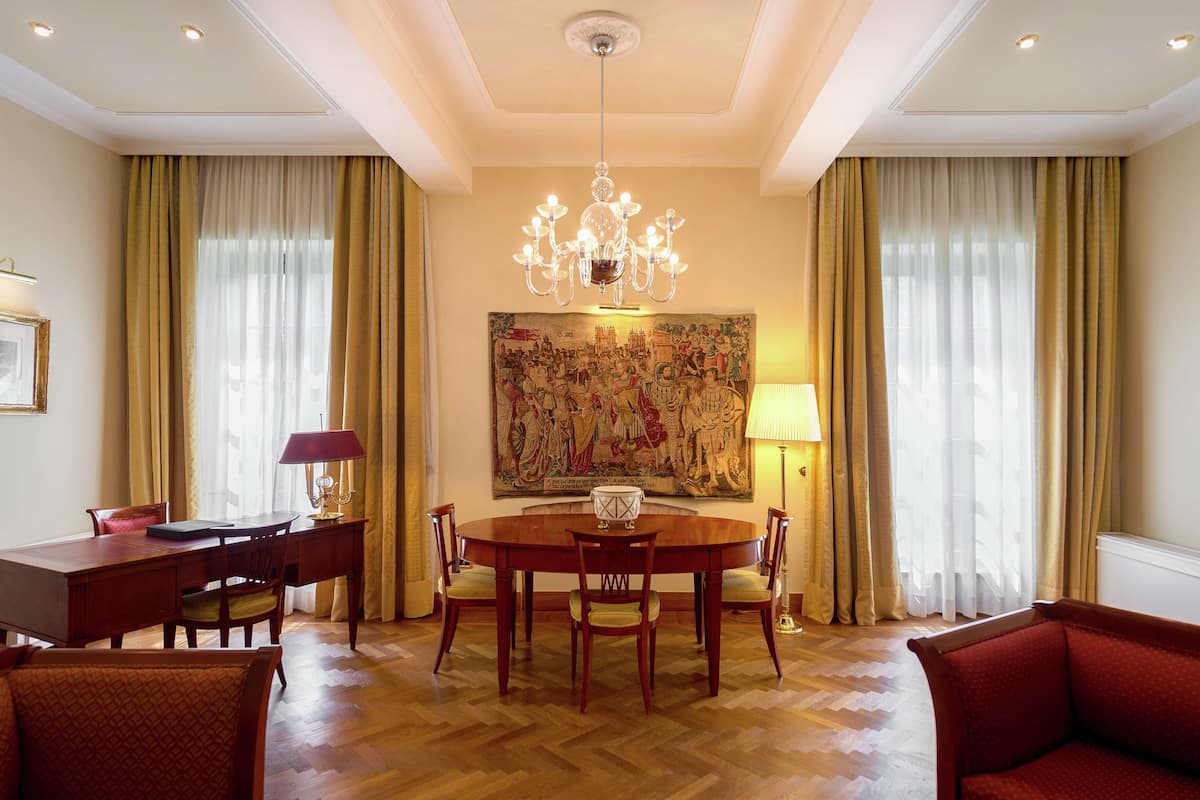 Ein Essbereich mit einem runden Tisch, Stühlen, einer Chandelierleuchtre und einem großen Gemälde an der Wand.