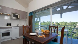 A modern kitchen with white cabinets, a microwave, and a dining area with a table set for two. - Madame Vacances Résidence Du Golf (Moliets-et-Maa)
