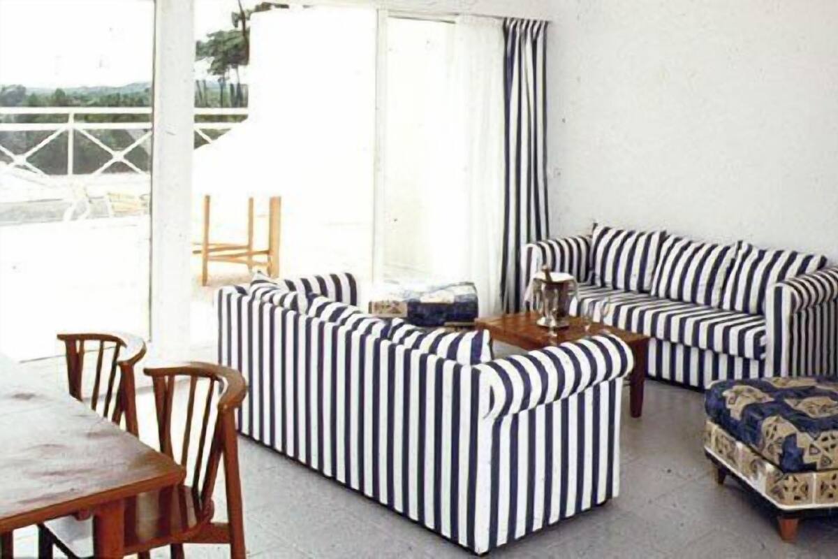 Ein Wohnzimmer mit einem gestreiften Sofagarnitur, einem Holztisch und einem Esstisch mit Stühlen.