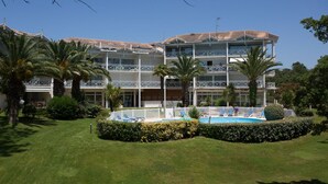 A multi-story hotel with a swimming pool, palm trees, and a well-maintained lawn. - Madame Vacances Résidence Du Golf (Moliets-et-Maa)