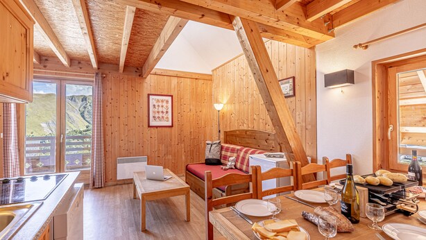 A cozy wooden cabin with a dining area, a bed with a red mattress, and a kitchen with a stove.