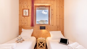 Une pièce chaleureuse aux murs en bois, une fenêtre donnant sur une montagne, deux lits, une petite table et une tablette posée sur l’un des lits.