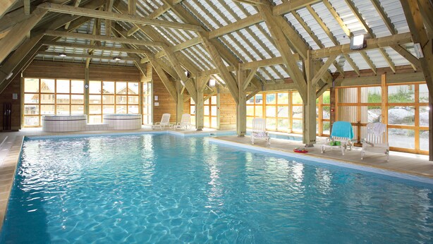 Une piscine intérieure avec des poutres en bois et de grandes fenêtres.