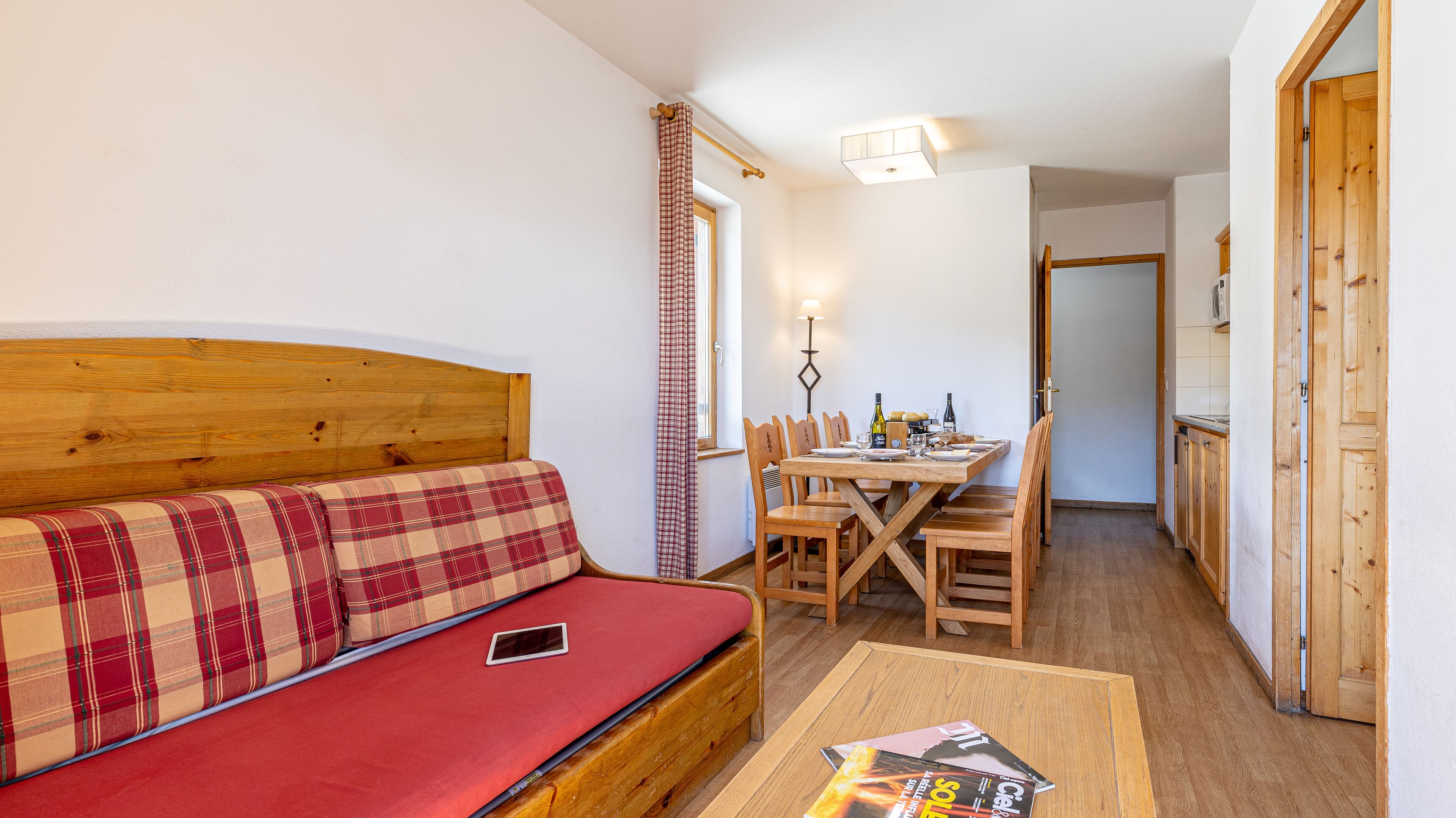 A cozy room with a wooden headboard sofa, a dining table with chairs, and a kitchen area.