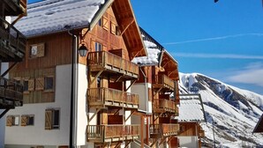 Un chalet en bois doté de plusieurs balcons, une montagne enneigée en arrière-plan et un ciel bleu dégagé.