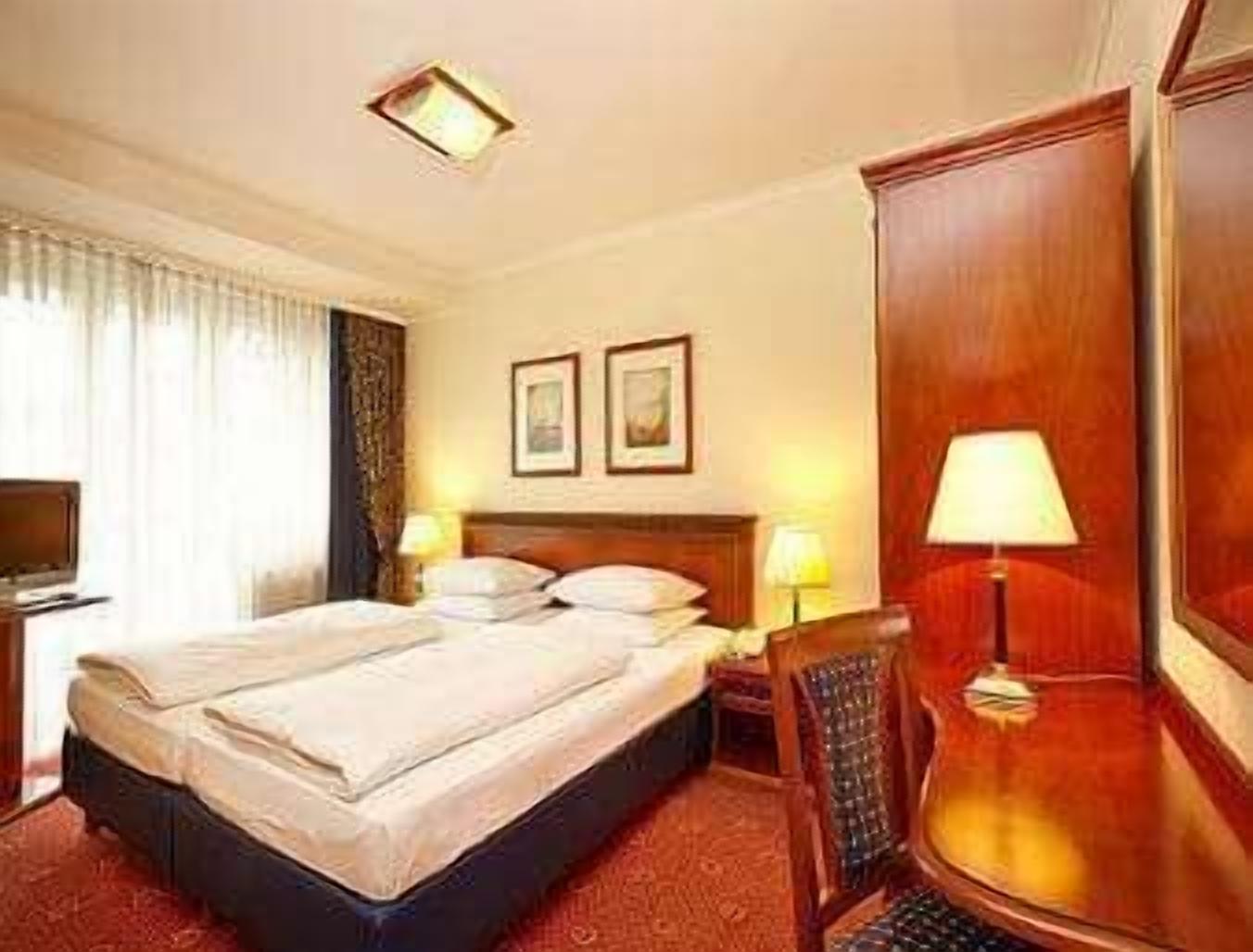 Una habitación de hotel con una cama, dos lámparas de noche, un televisor y un armario de madera.