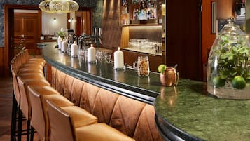 A bar area with leather barstools, a marble countertop, and a variety of bottles and glasses.