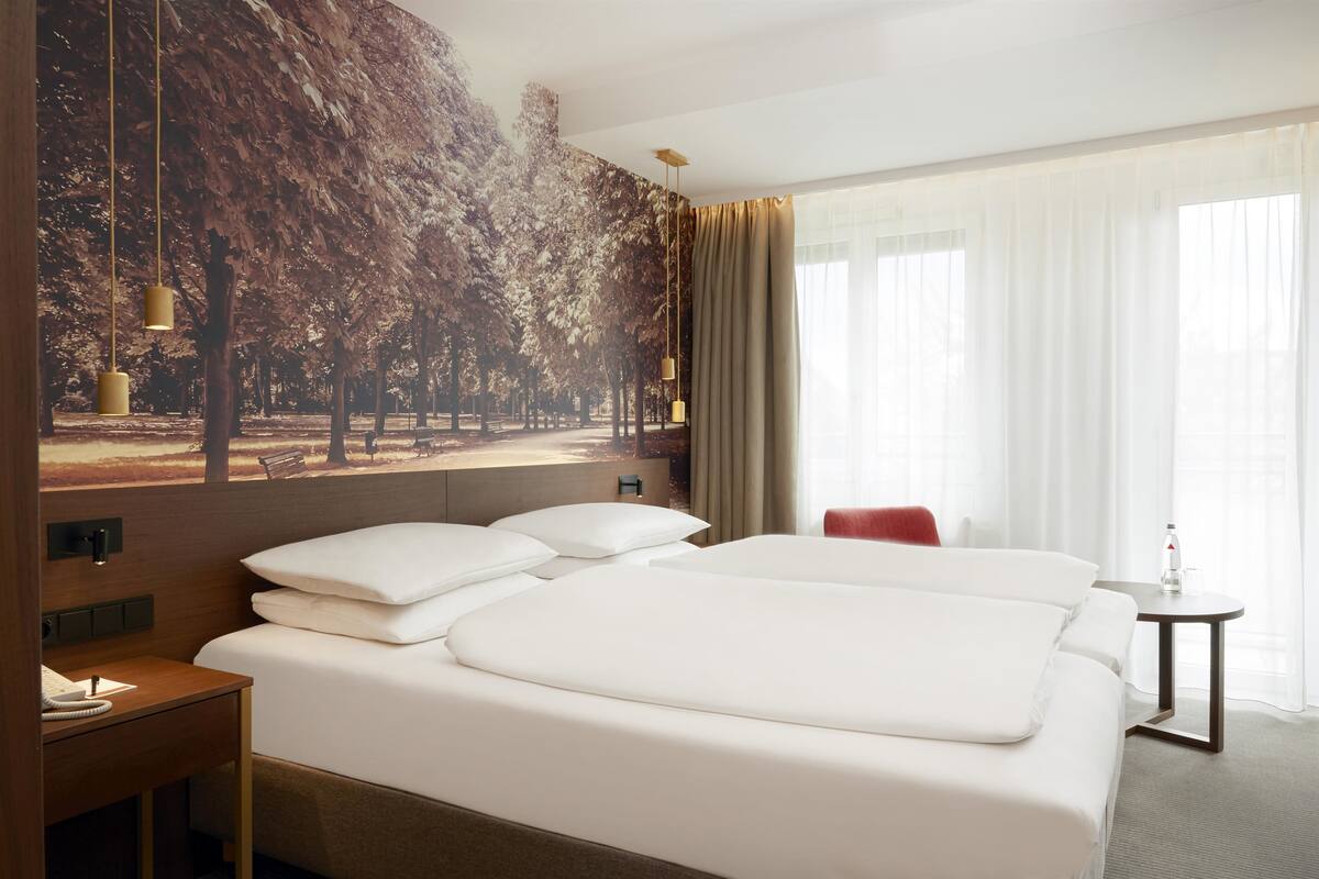 A hotel room with a large bed, a small table, a chair, and a wall-mounted TV.