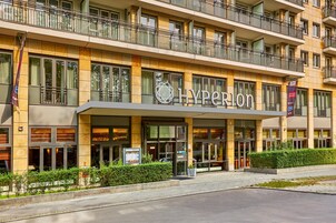 Ein Hotel mit moderner Fassade, einem markanten 'Hyperion'-Schild und einem gepflegten Eingangsbereich mit kleinem Garten.