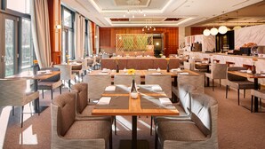 A spacious hotel dining area with multiple tables and chairs, a central seating area, and a kitchen counter. - HYPERION Hotel Berlin (Berlin)