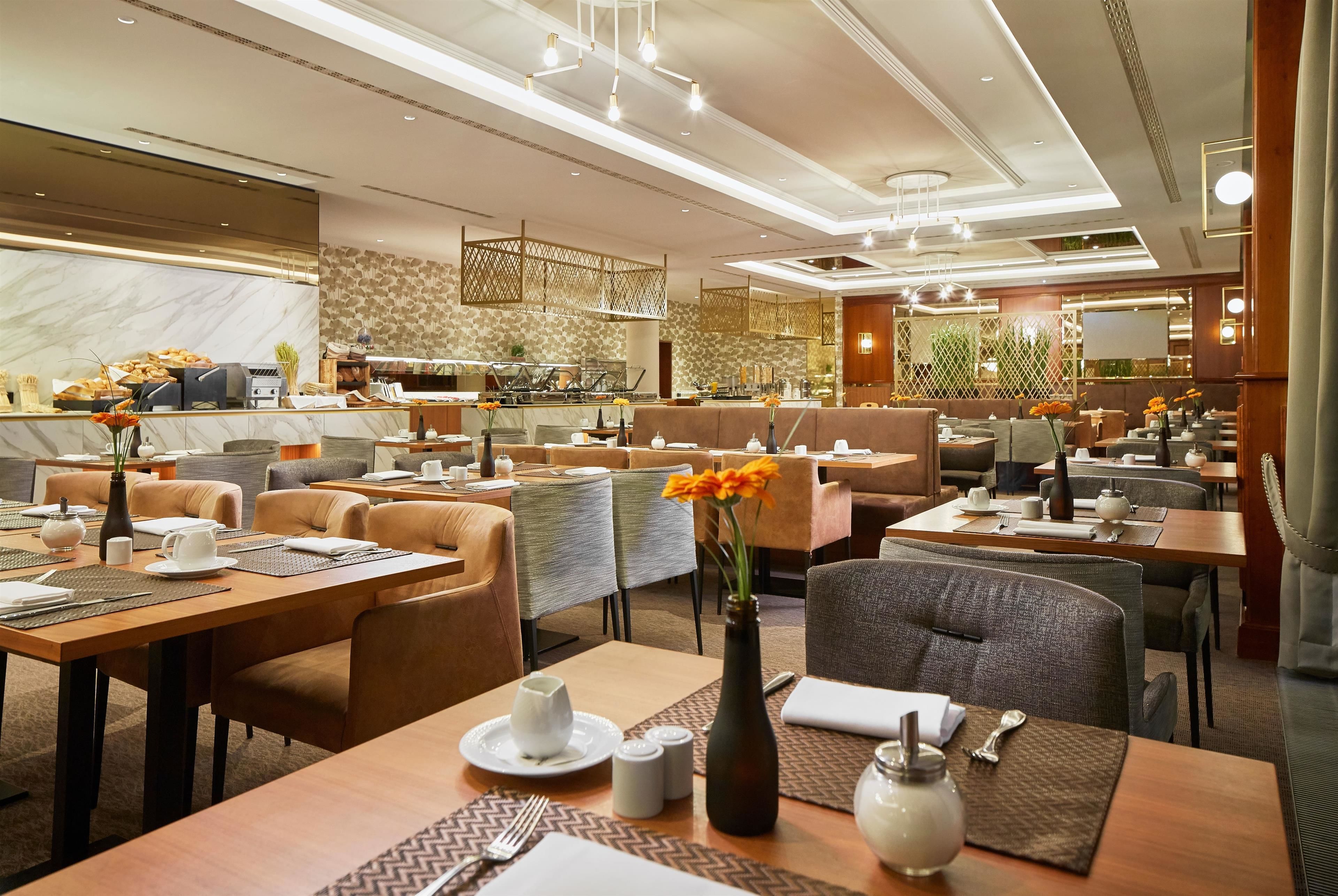Ein modernes Restaurant mit verschiedenen Essbereichen, darunter eine Bar und Sitzgelegenheiten mit Tischen und Stühlen.