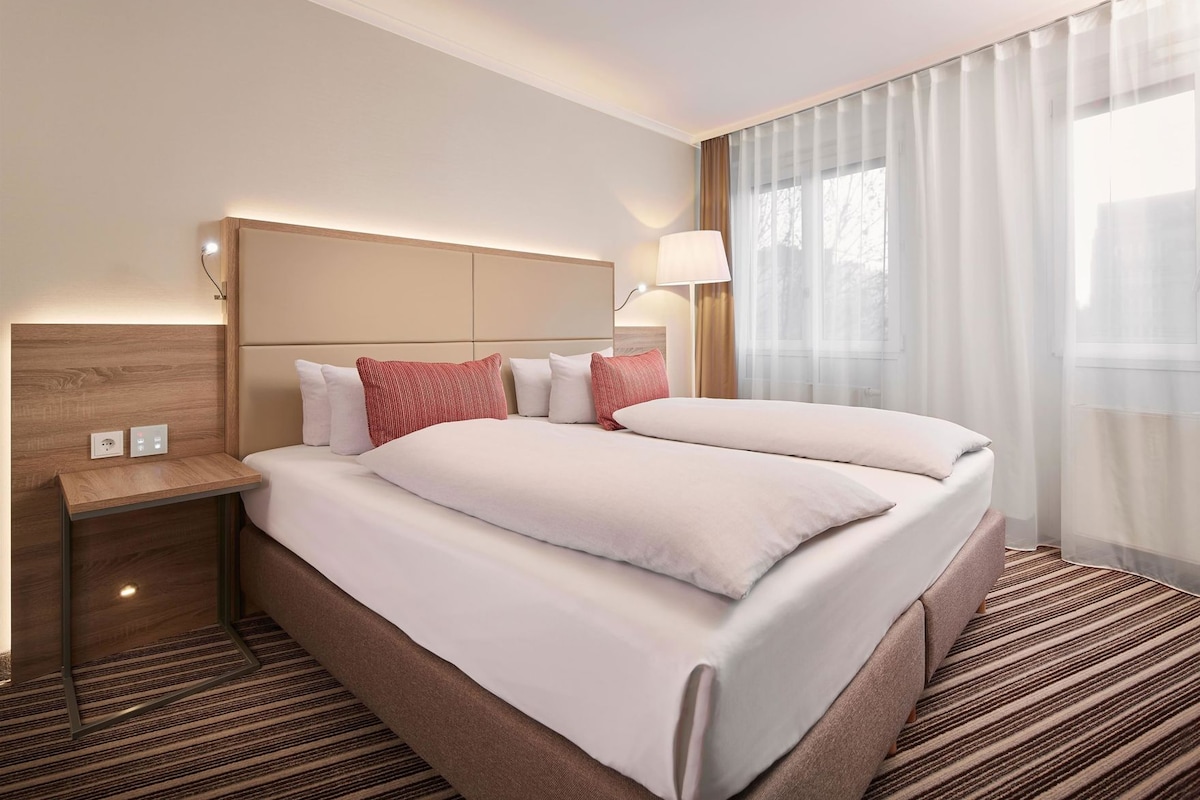 A hotel room with a bed, bedside tables, a lamp, and a window with curtains.