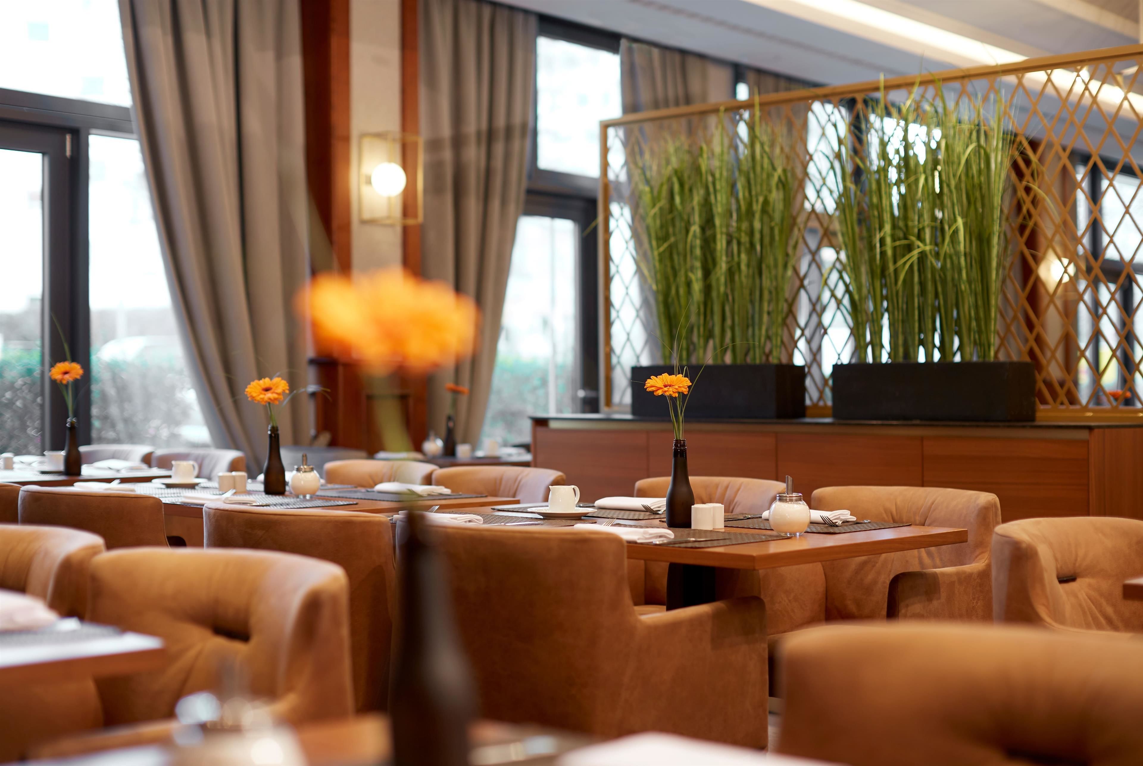 A hotel dining area with tables set for dining, chairs, and potted plants.