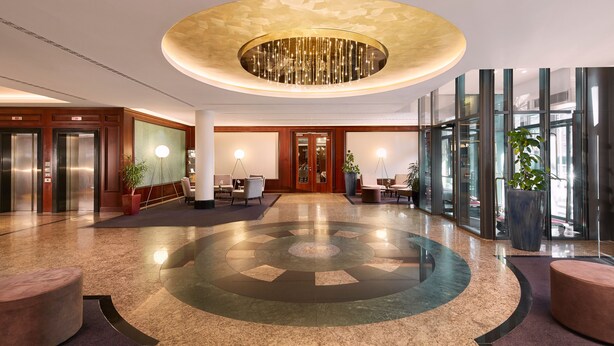A modern lobby with a circular patterned floor, elevators, seating areas, and large windows. - HYPERION Hotel Berlin (Berlin)