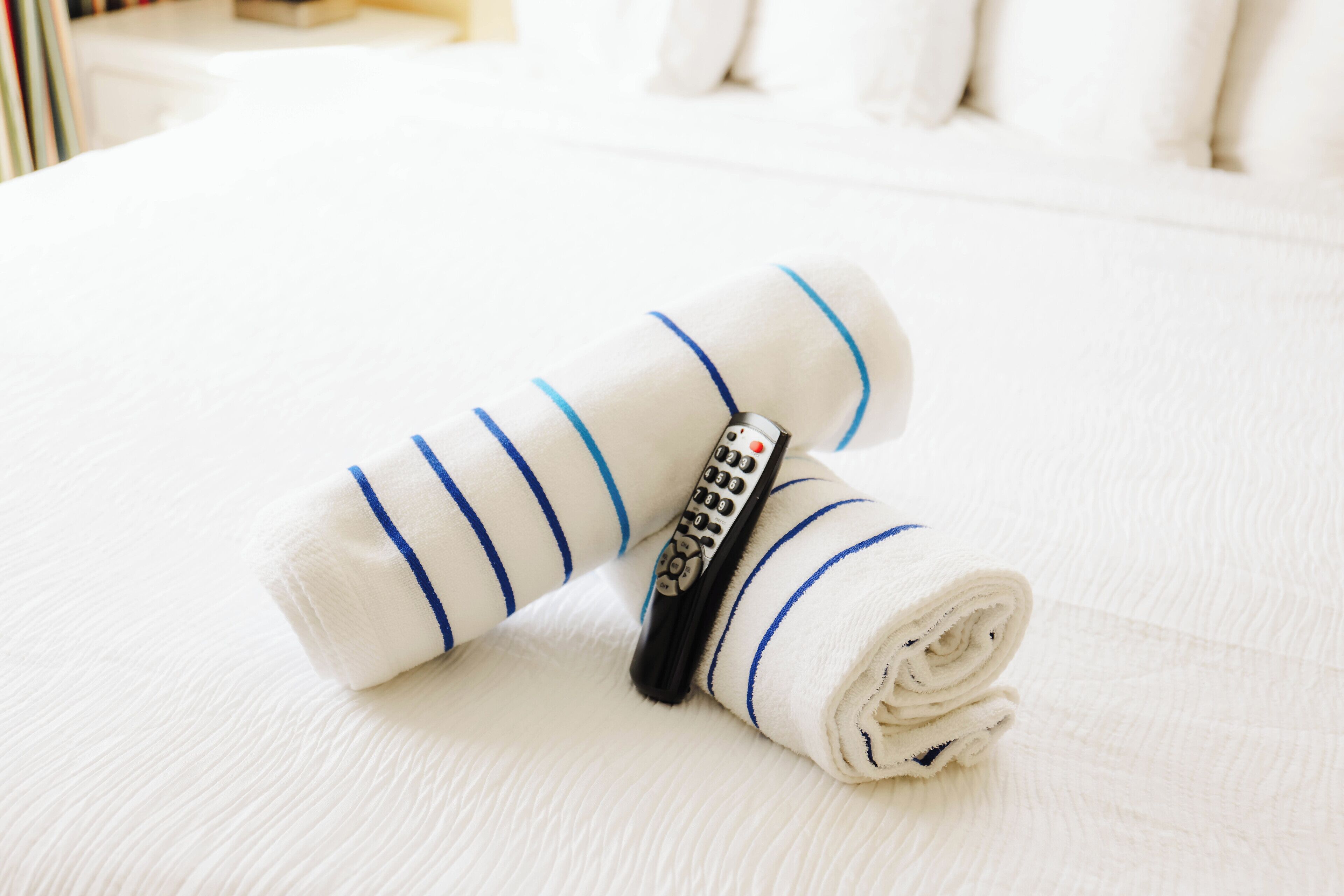 A neatly folded white towel with blue stripes and a remote control on a bed.