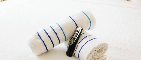 A neatly folded white towel with blue stripes and a remote control on a bed.