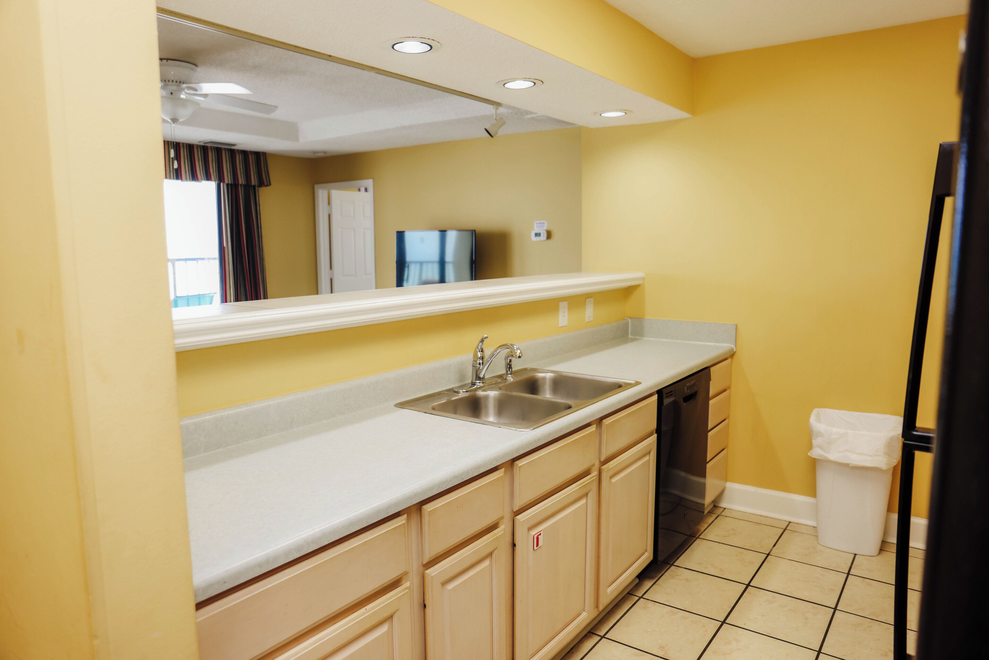 A kitchen with a white countertop, stainless steel sink, and beige cabinets.