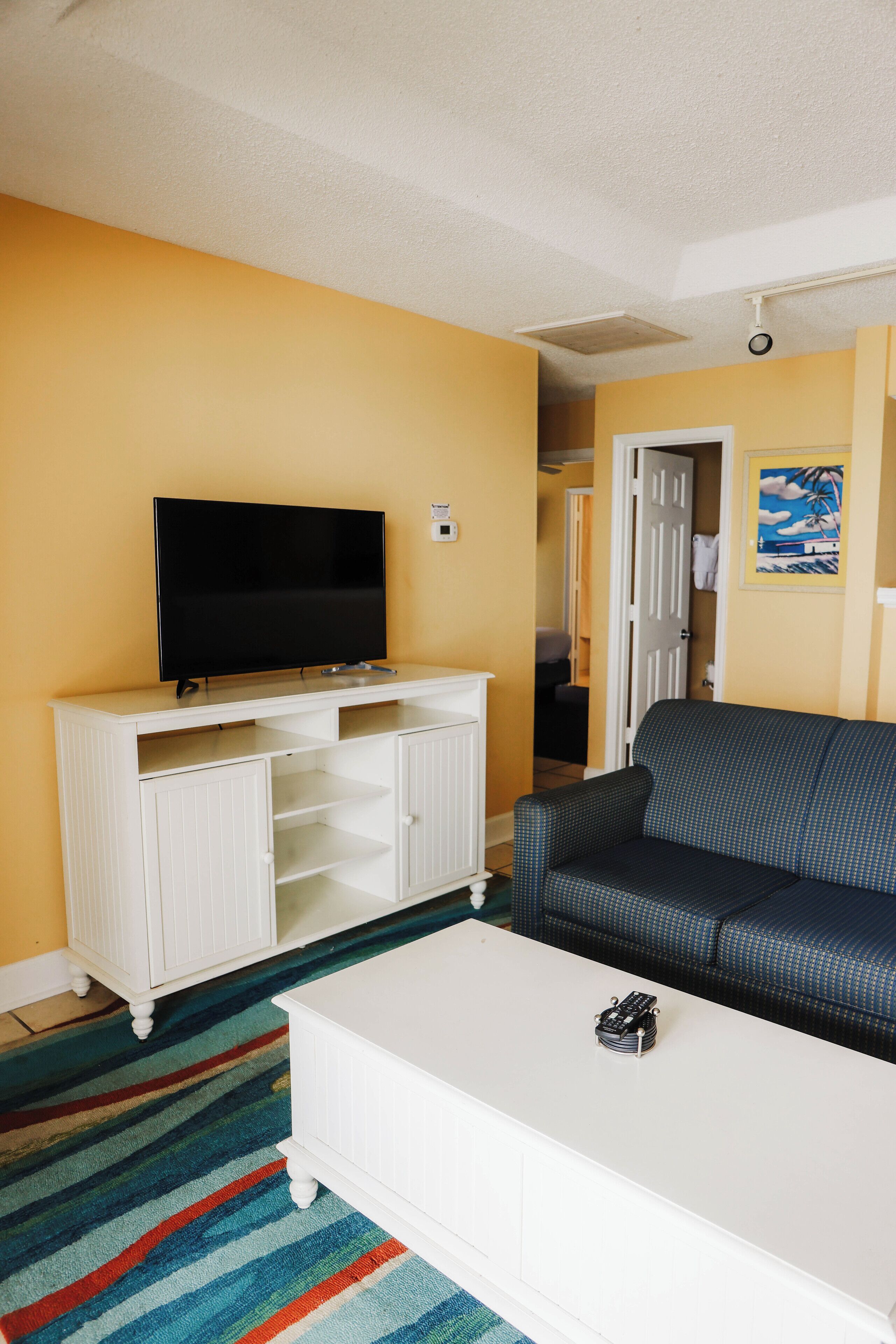 A living room with a flat-screen TV on a white entertainment unit, a blue patterned sofa, and a white coffee table.