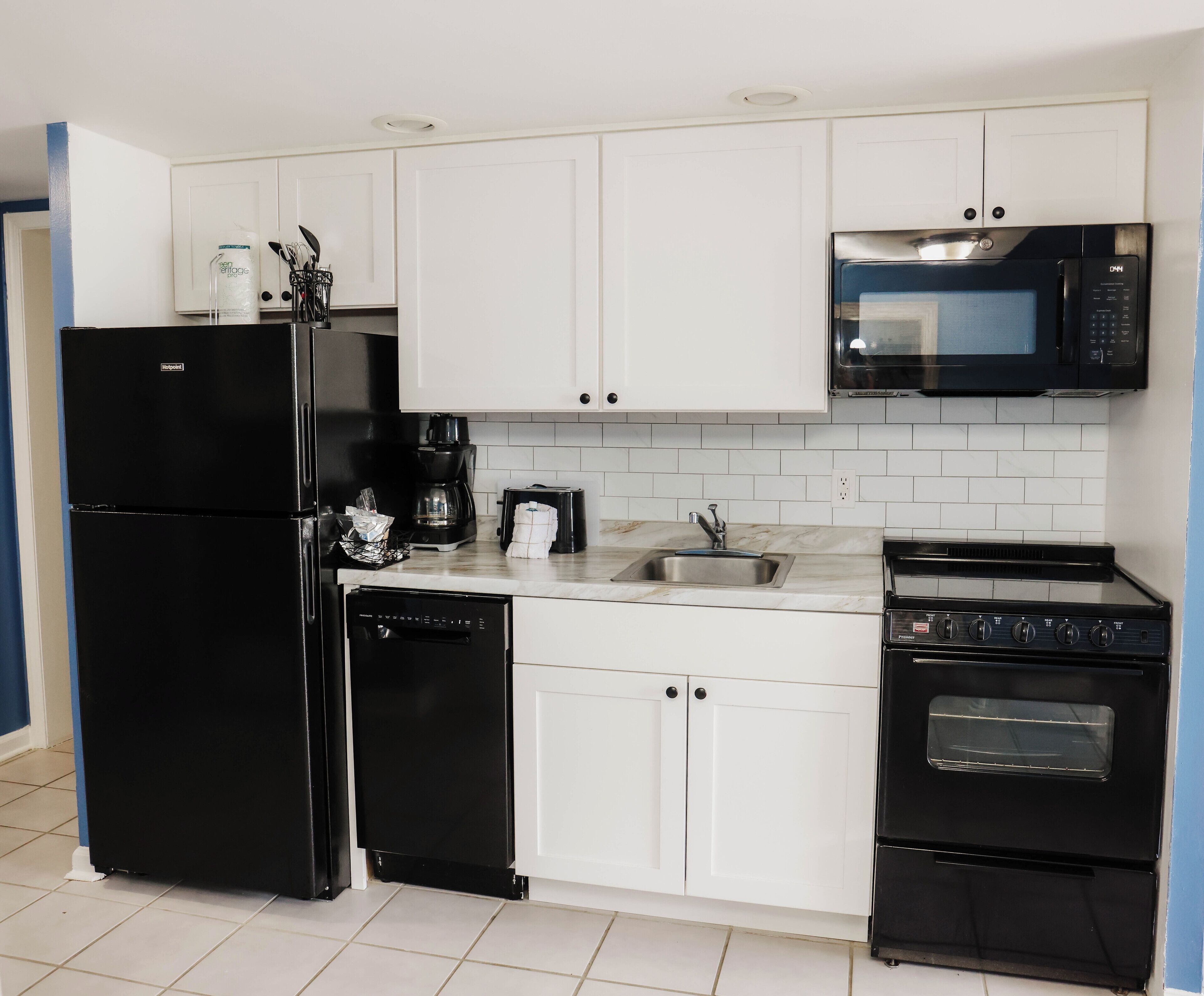 A compact kitchen with a black refrigerator, a coffee maker, a microwave, a dishwasher, and a stove.