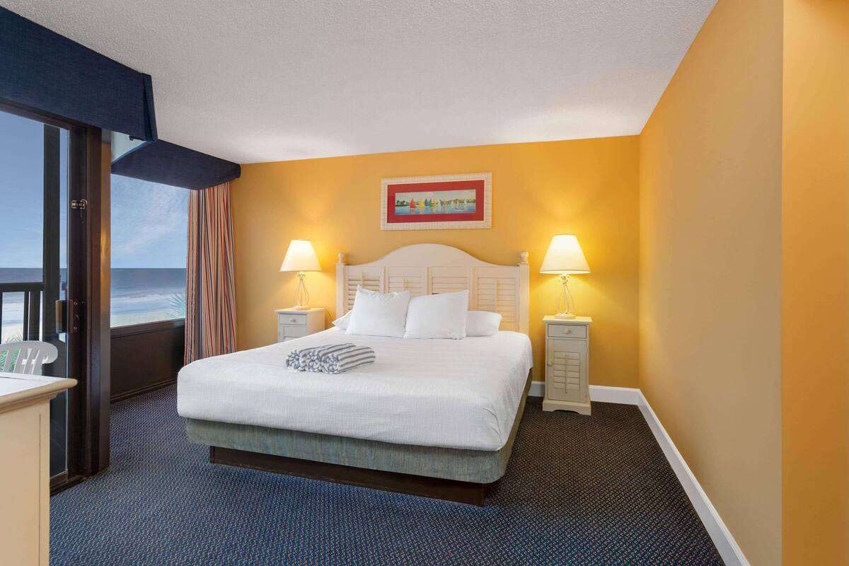 Hotelkamer met een bed, twee bedlampen, een schilderij aan de muur en uitzicht op de oceaan door een raam.