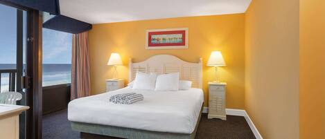 A hotel room with a bed, two bedside lamps, a painting on the wall, and a view of the ocean through a window.