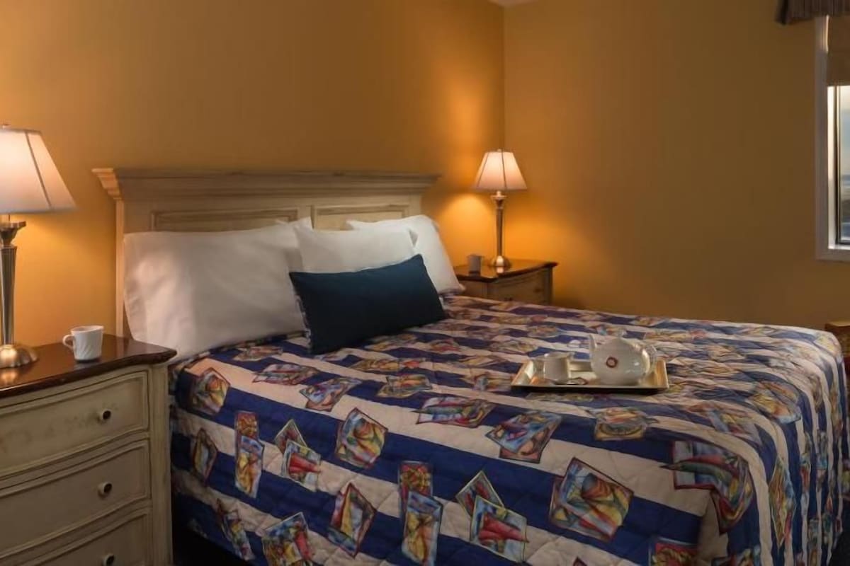 Een hotelkamer met een bed, twee bedlampen, een nachtkastje, een stoel en een raam met uitzicht.