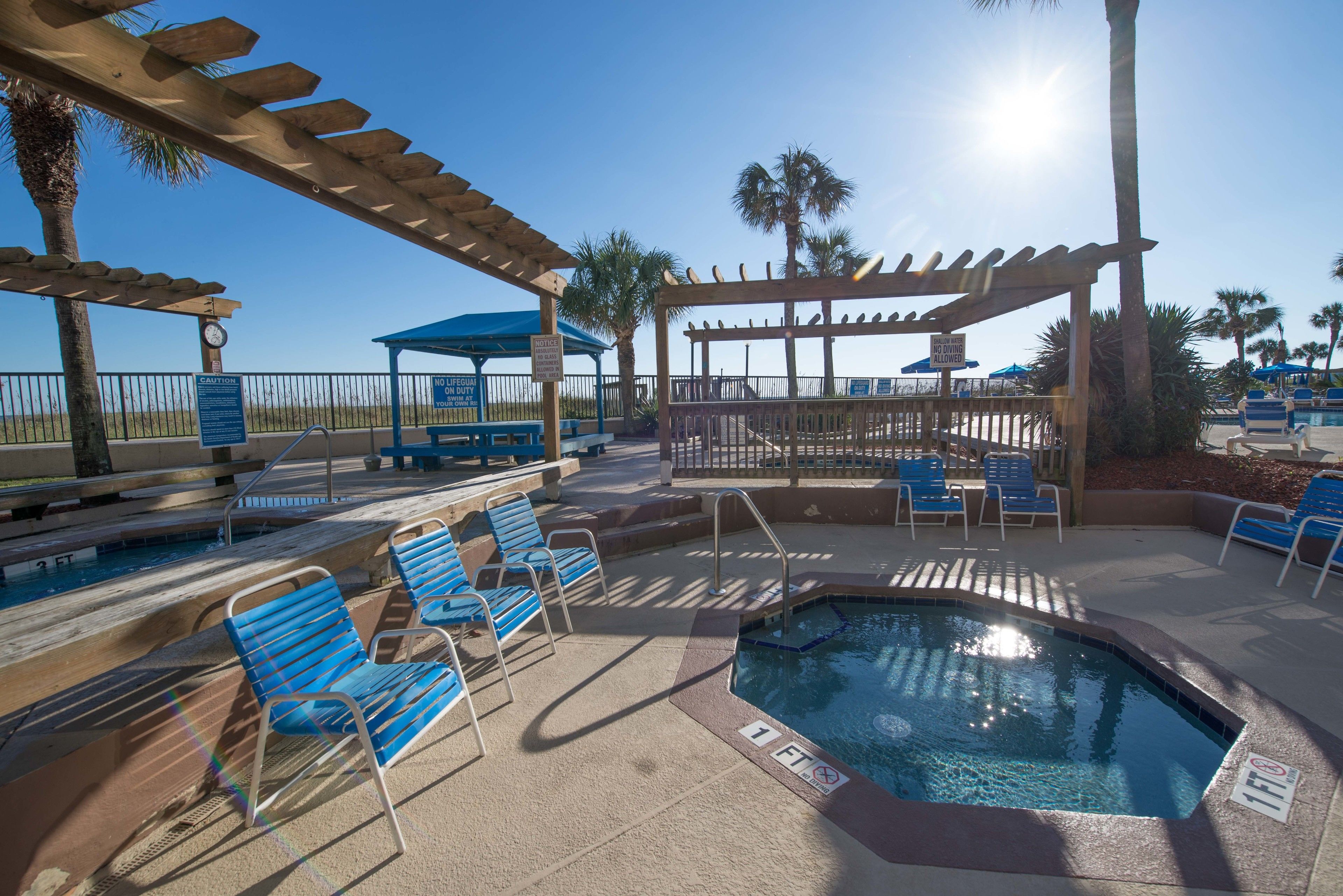 A pool area with blue chairs, a hot tub, and a pergola.