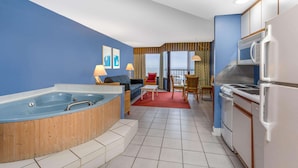 A modern hotel room with a jacuzzi, a dining area, and a kitchenette.