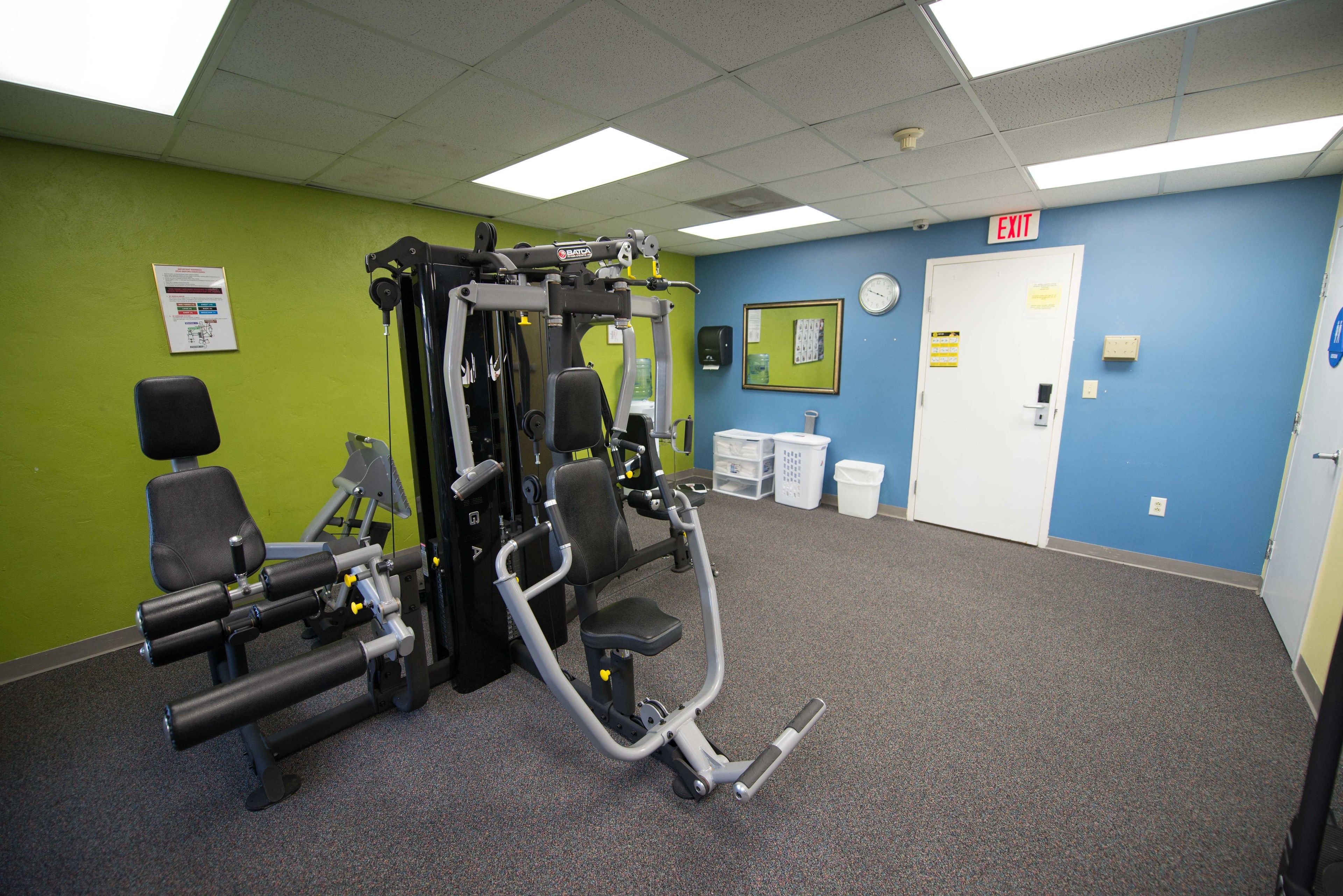 A gym with exercise equipment, a green wall, a blue wall, and an exit sign.