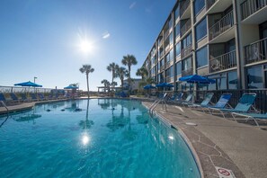 A swimming pool with lounge chairs and umbrellas, surrounded by a multi-story building with balconies.