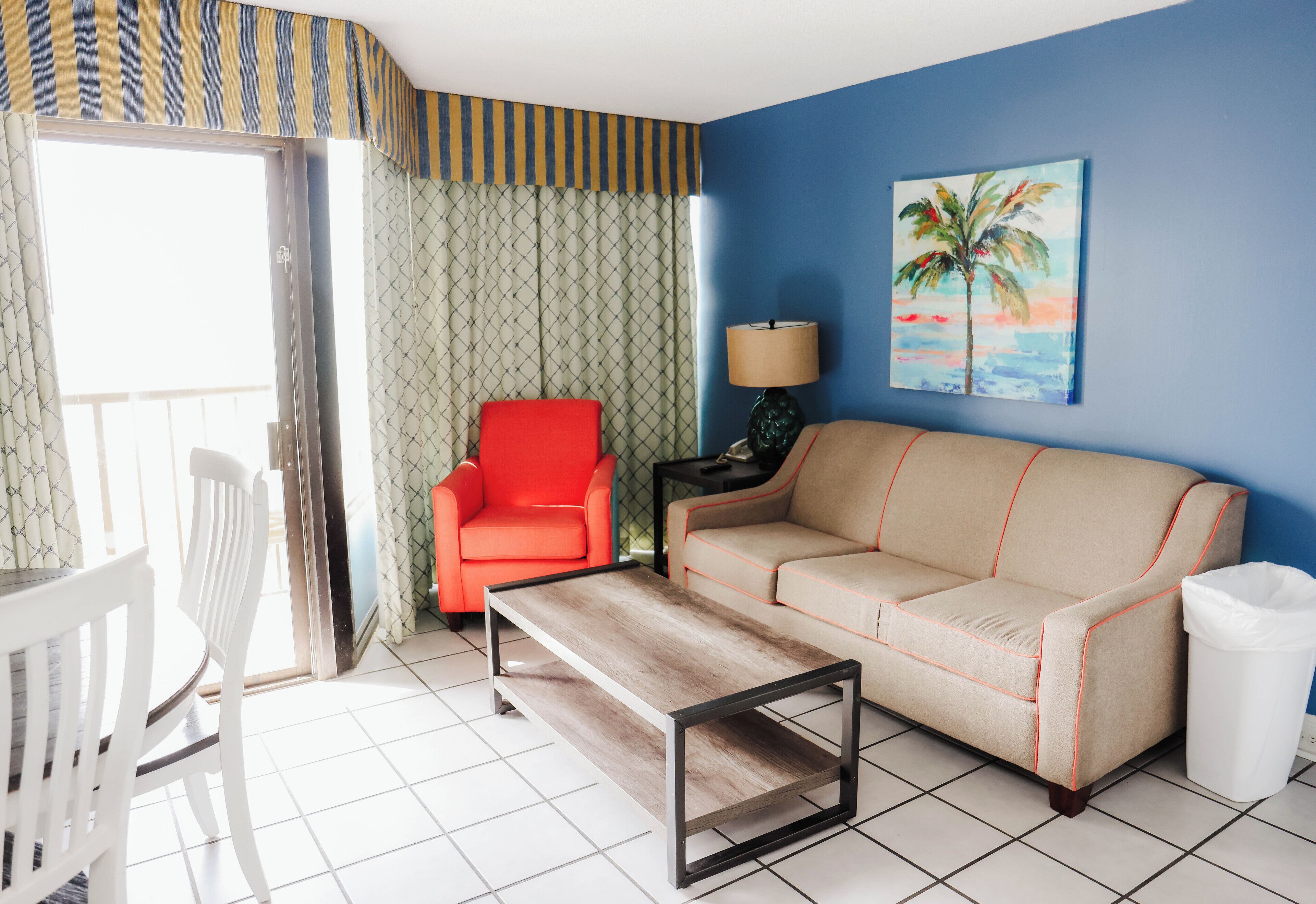 A room with a sofa, a red chair, a wooden coffee table, a lamp, and a painting on the wall.
