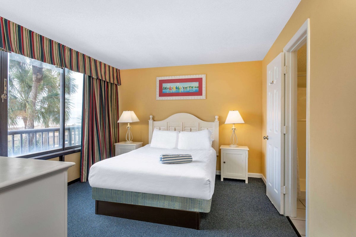 Hotelkamer met een bed, twee nachtkastjes met lampen, een raam met gordijnen, een schilderij aan de muur en een deur.