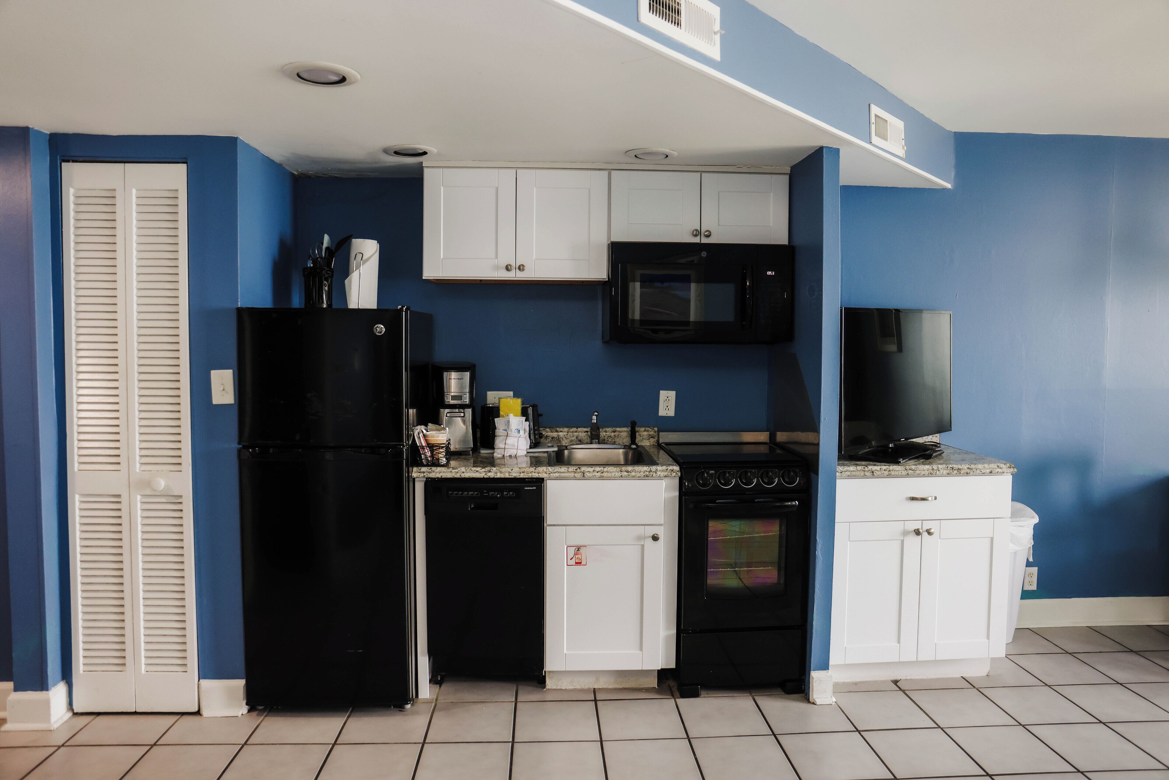A compact kitchen with white cabinets, a black refrigerator, a microwave, and an oven.