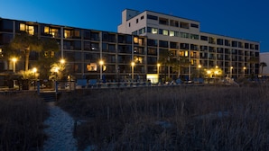 A multi-story hotel with balconies, a beach path, and outdoor seating.