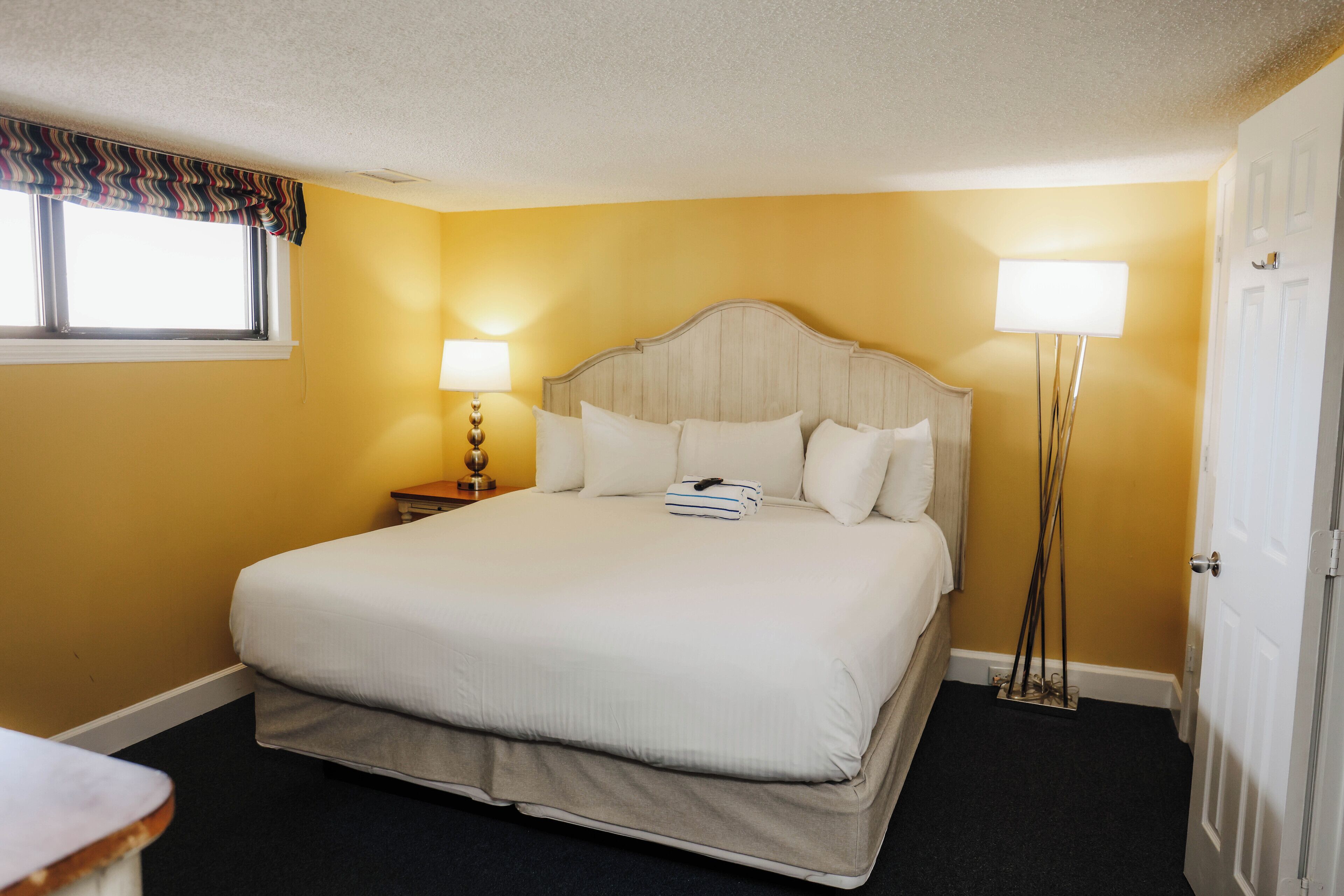 Une chambre d’hôtel avec un grand lit, deux lampes de chevet, une fenêtre avec un rideau et une porte.