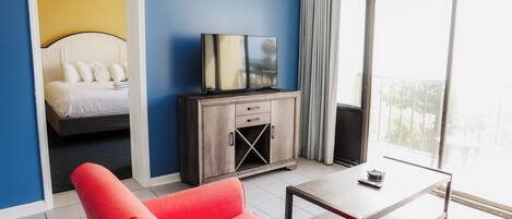 A hotel room with a bed, a television, a red chair, a small table, and a view of the outdoors.