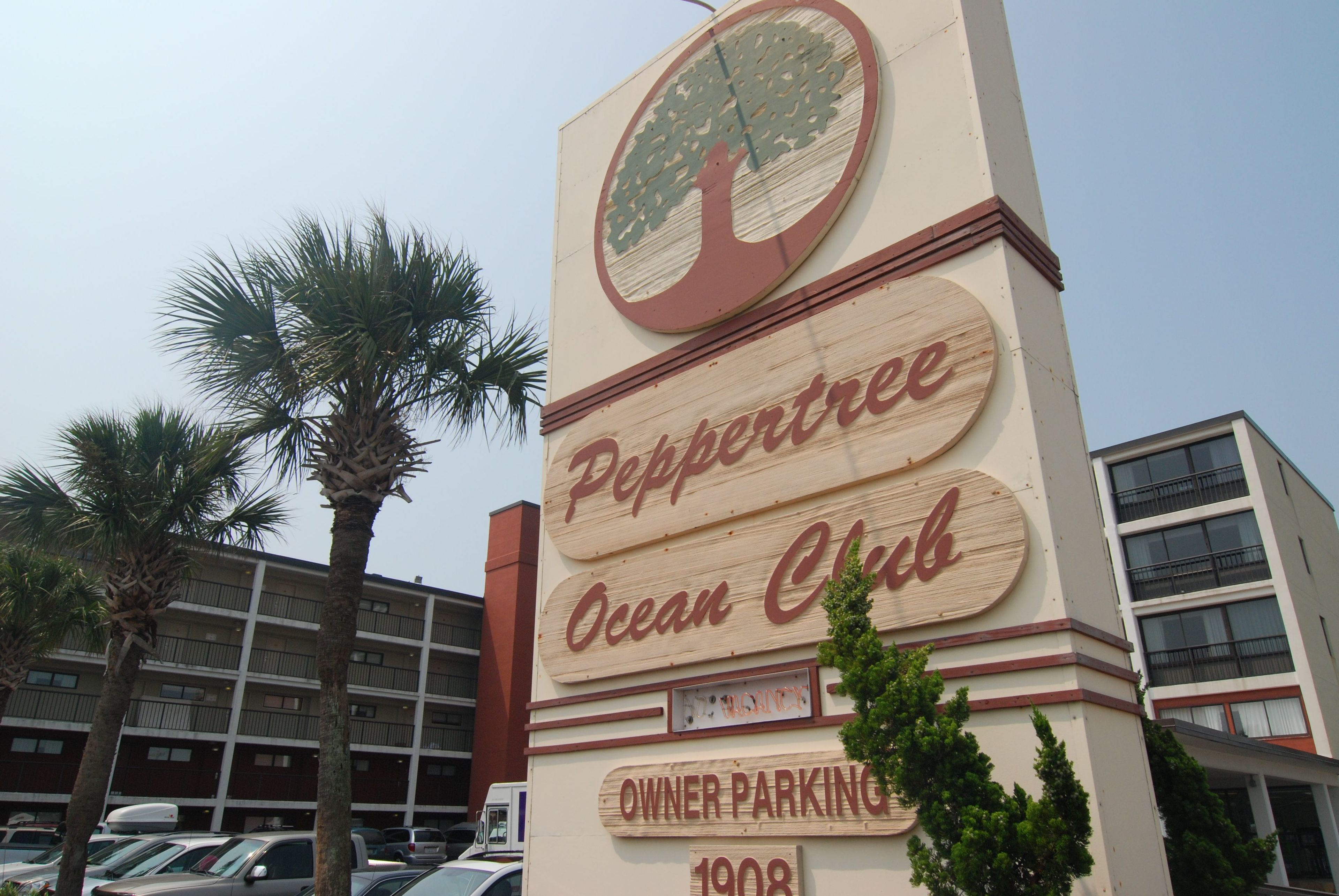 Señal para el Peppertree Ocean Club con un gran logotipo de árbol, indicando estacionamiento para propietarios.