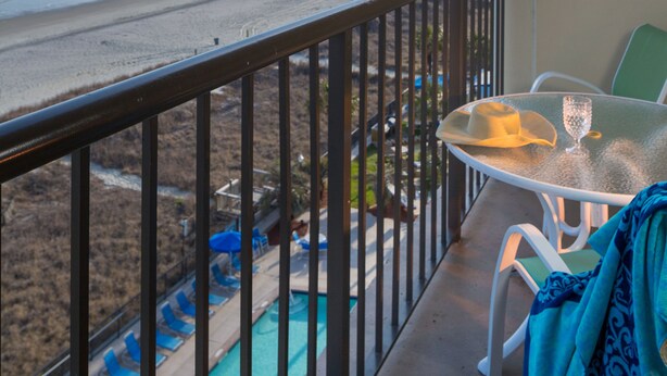 A balcony with a view of the beach and ocean, a pool, and outdoor seating.