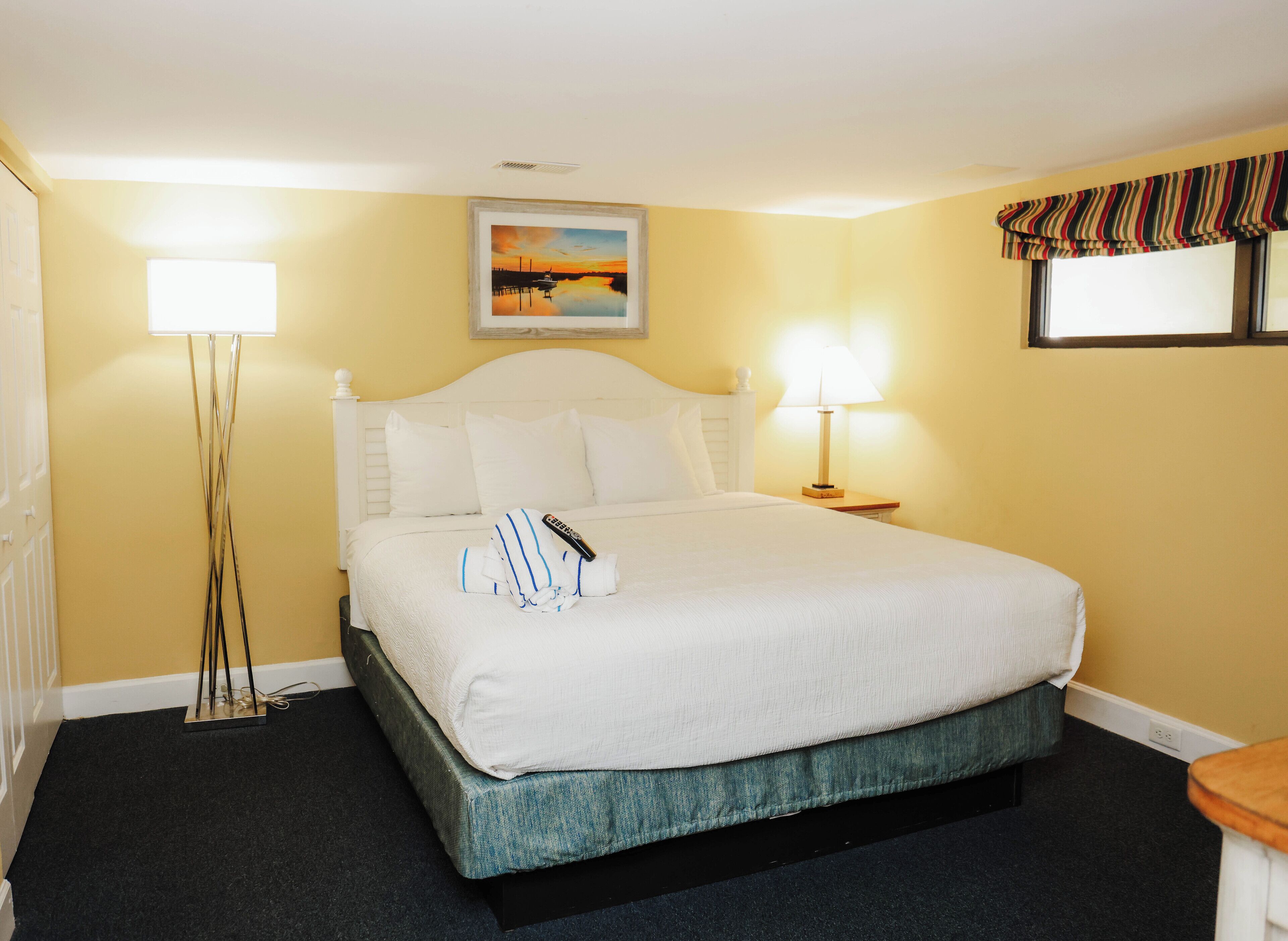 Habitación de hotel con cama, lámparas de noche, un cuadro en la pared y una ventana con cortina a rayas.
