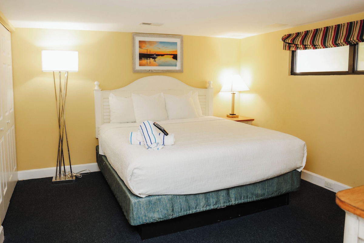 Quarto de hotel com cama, abajures, um quadro na parede e janela com cortina listrada.