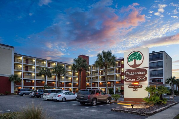 A hotel with a sign for 'Peppertree Ocean Club' and a parking lot with several cars.
