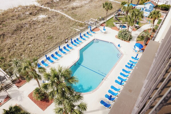 An aerial view of a resort with a swimming pool surrounded by lounge chairs and palm trees.