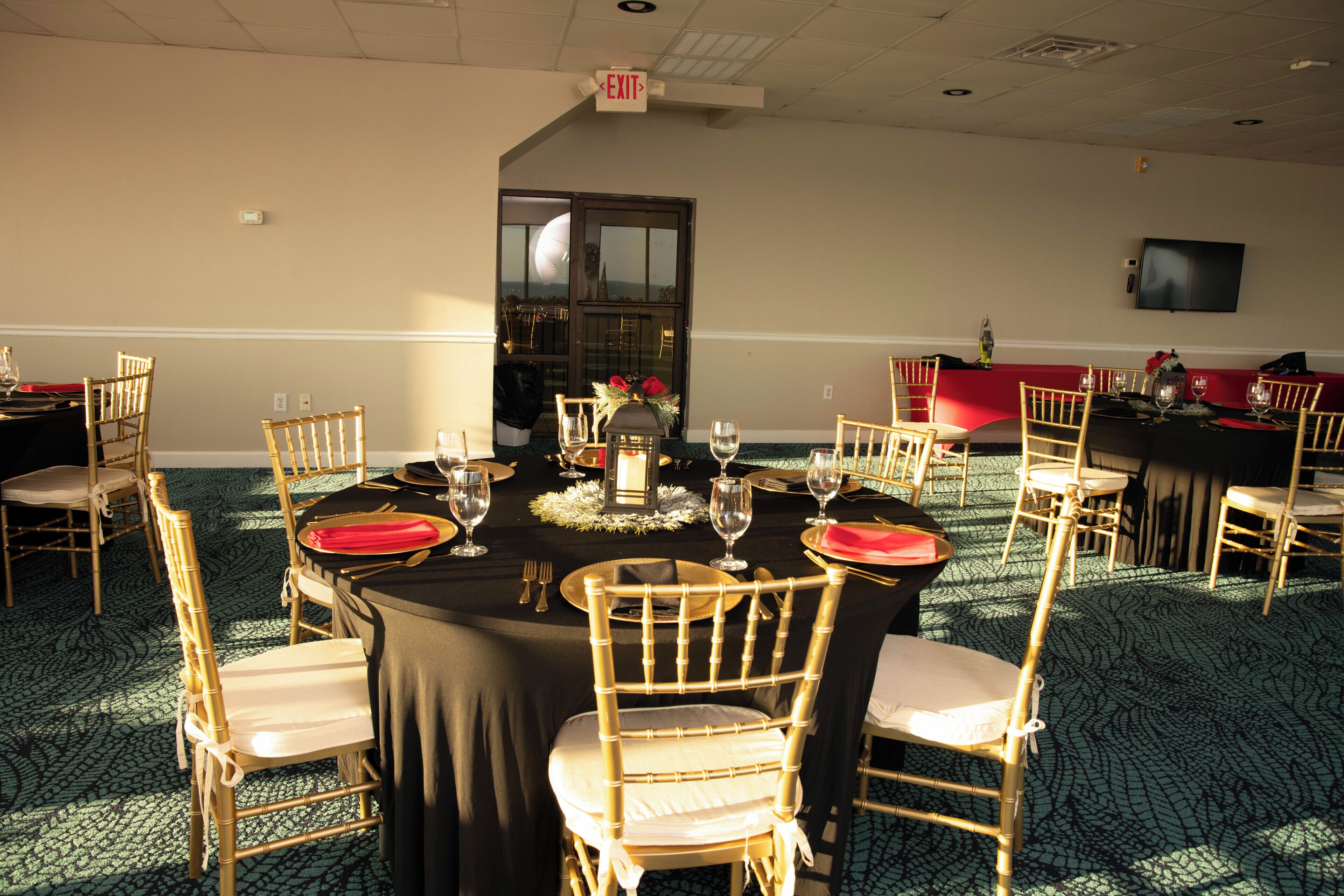 A banquet hall with round tables, chairs, and a television on the wall.
