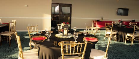 A banquet hall with round tables, chairs, and a television on the wall.