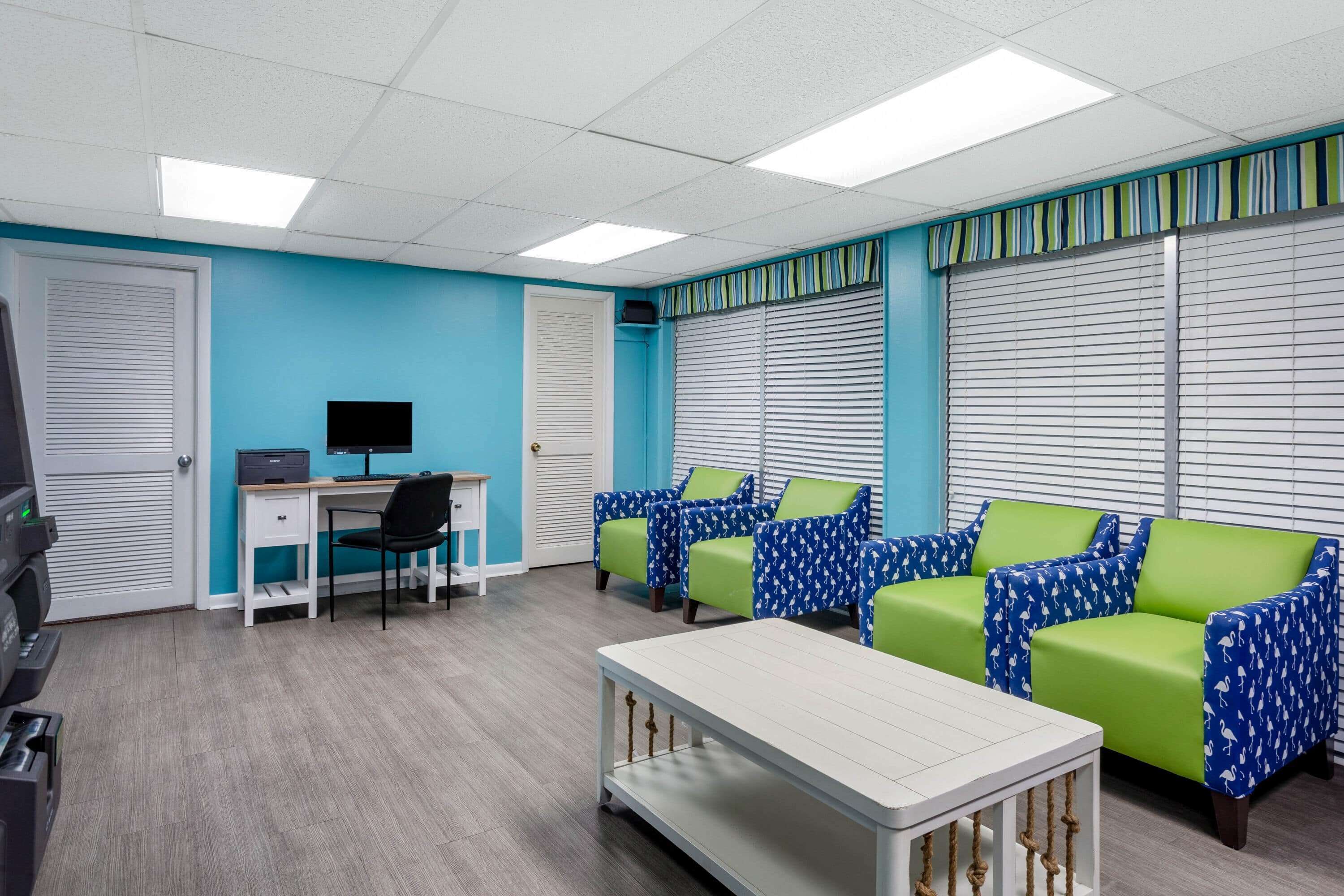 A room with a desk, computer, and two green and blue patterned sofas.