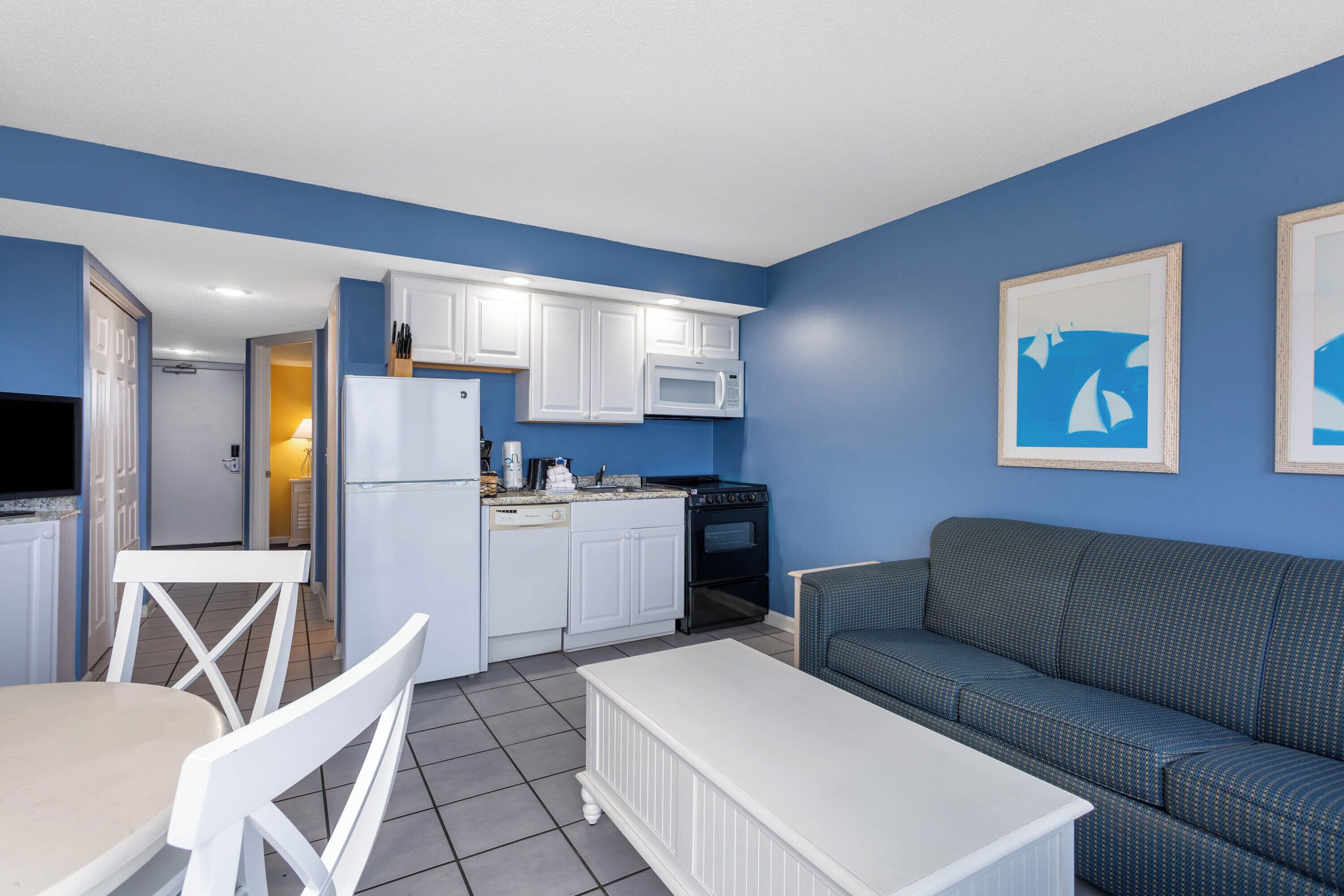 A compact living space with a kitchenette, a dining area with white furniture, and a blue sofa.